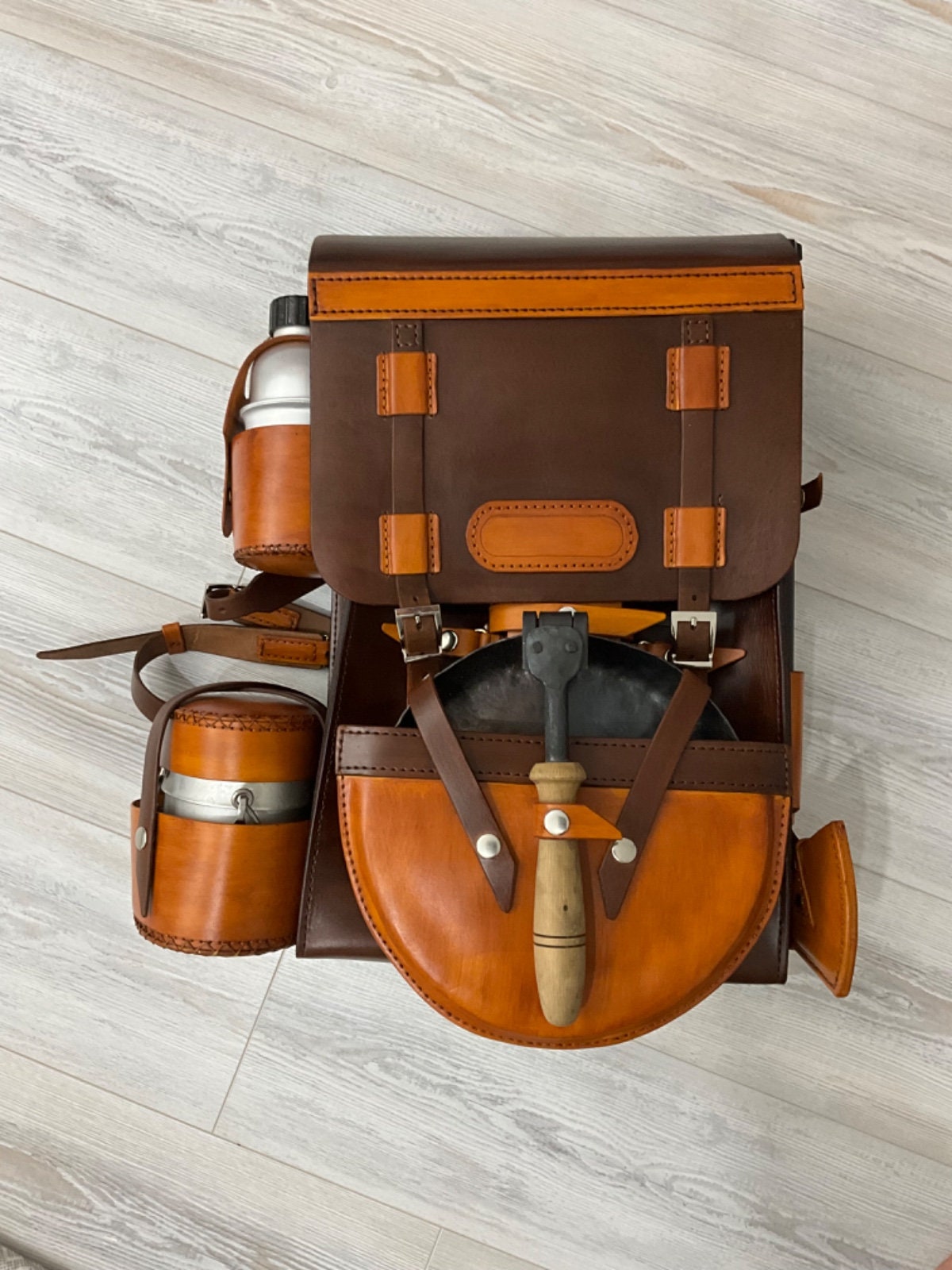 Handmade leather bushcraft bag a bushcraft axe, handmade folding pan, aluminum water carrier, camping pot, bushcraft drill, and bowsaw